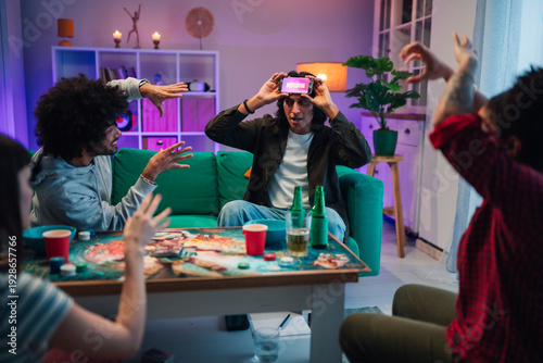 Canvas Print Diverse friends having fun playing charades game at home party, using mobile pho