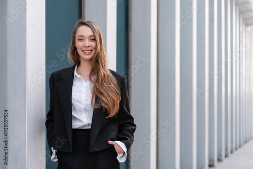 Cuadro en lienzo Smiling businesswoman in black suit standing against modern architectural columns