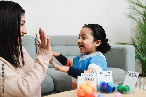 Asian kid playing didactic game with his mom at home - Montessori education concept - Focus on mother face