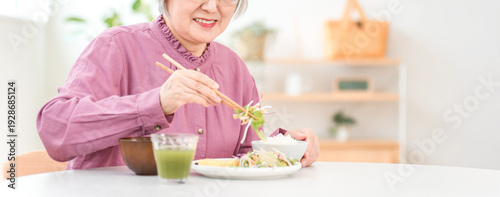 A gray-haired senior woman eating in the dining room at home