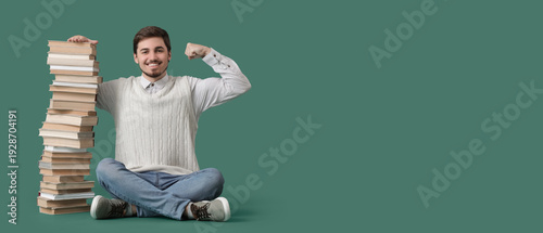 Young man with stack of books showing muscles on green background