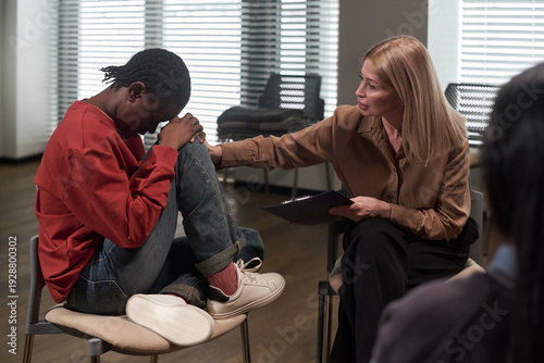 Foto Caucasian middle aged woman comforting Black teenager sitting with knees up and