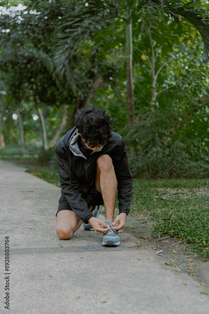 Fototapeta premium Portrait of handsome asian man posing fixing shoelace lace on his running shoe after exercising outdoors. Vitality and activity concept.