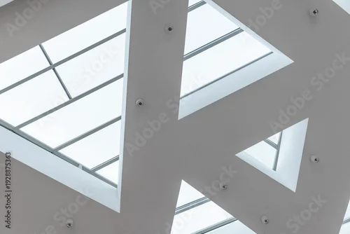 Fototapeta na wymiar A modern minimalist ceiling features geometric triangular skylights that flood a contemporary interior with soft natural light, emphasizing clean lines, negative space and architectural abstraction
