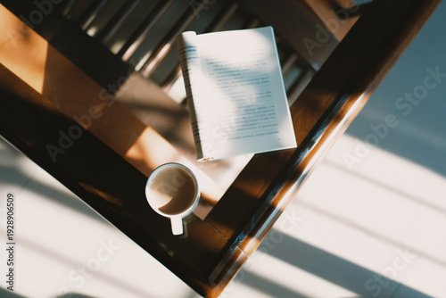 Open book and coffee cup on wooden table with sunlight beams casting shadows