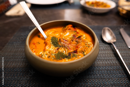 Indian Curry Bowl with Spices and Herbs Served on Dark Tablecloth in Restaurant Setting