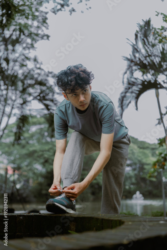 Portrait of handsome asian man posing fixing shoelace lace on his running shoe after exercising outdoors. Vitality and activity concept.