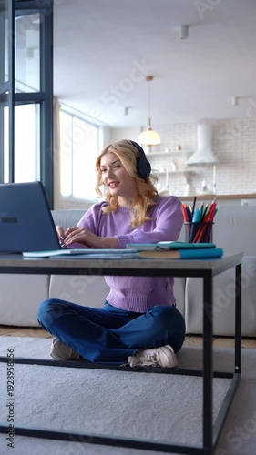 Smart attractive blonde female high school student in wireless headphones preparing for exam, studying distant online course and communicating with teacher while-learning at home.