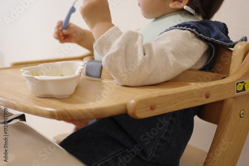 Photos Toddler sitting in a wooden high chair during mealtime at home