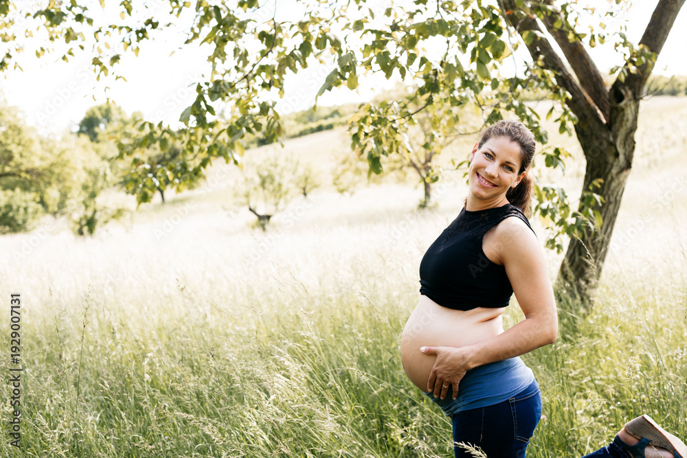 © Westend61 - Young pregnant woman holding baby belly, standing on a meadow © Westend61 - Young pregnant woman holding baby belly, standing on a meadow