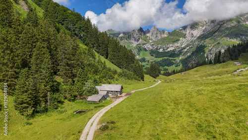Aerial, bird view, Easy hiking trail, dirt road with some hikers walking towards mountains. Hiking path in green valley in Swiss Alpstein mountains. Wooden cabin in Switzerland mountains. Hiking outdo