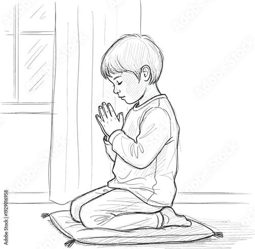 A young boy sits cross-legged on a mat in prayer indoors with hands clasped