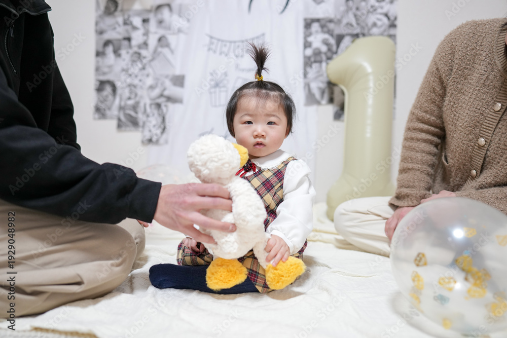 Fototapeta premium A baby is sitting on a bed with a stuffed duck. A man is holding the baby's hand