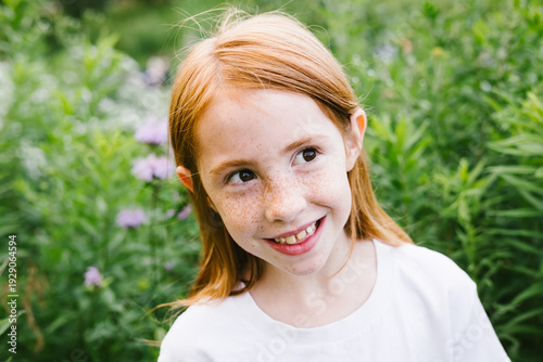 Happy red hair girl with freckles outside by field of purple flowers