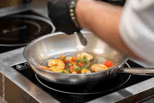Fotografija A chef wearing black gloves is cooking shrimp with cherry tomatoes and fresh her