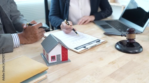 Lawyers reviewing a contract with a house model and gavel on the desk, representing real estate legal consultation, property agreement, and home ownership documentation.