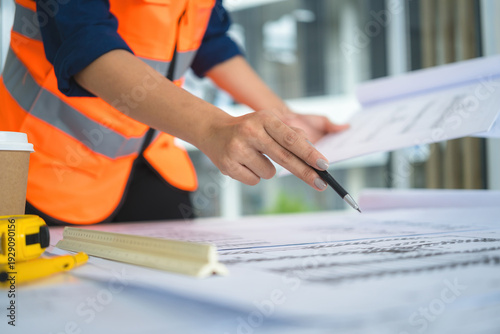 Female Asian Engineer in Safety Vest Reviewing Blueprints