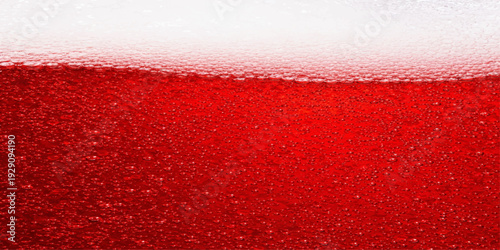 A macro shot captures the golden refreshment of a cold beverage as bubbles and foam swirl within a close up of a red wine glass, creating an abstract liquid display of gold and white froth