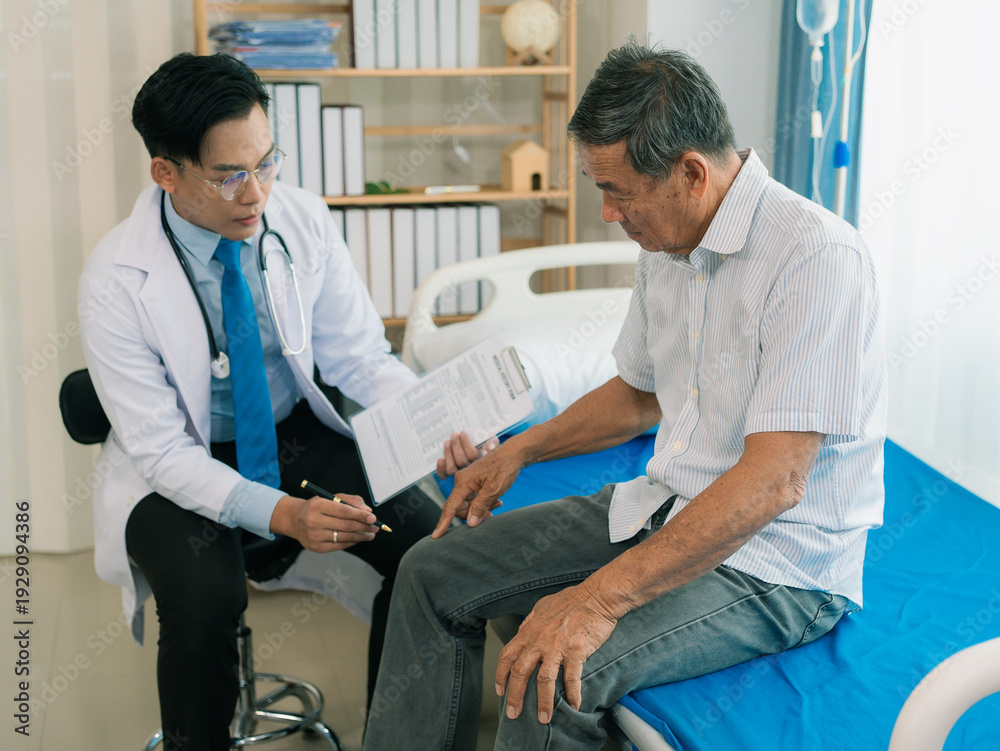 Obraz premium An Asian male doctor is examining an elderly male patient lying on a bed in a hospital ward, a healthcare concept.