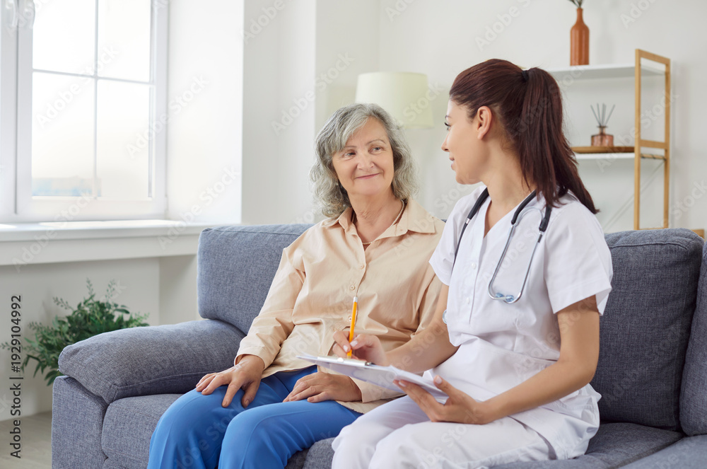 Obraz premium Senior woman in living room of nursing home talking to doctor, close-up. Nurse writing down symptoms of elderly patient. Concept checkup, health care, retirement home, healthcare and medicine