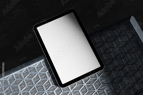 A sleek tablet with a blank white screen rests on a textured, honeycomb-patterned surface, set against a dark background