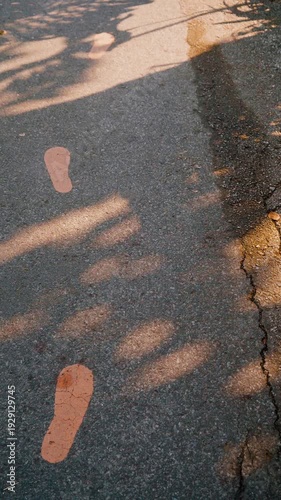 Camera footage of painted footprints on asphalt road with warm golden sunlight and natural tree shadows. Concept of journey, direction, walking path and lifestyle movement.