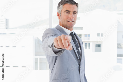 Wallpaper Mural Man in 40s standing in bright office by floor-to-ceiling windows, wearing light gray suit, pointing Torontodigital.ca