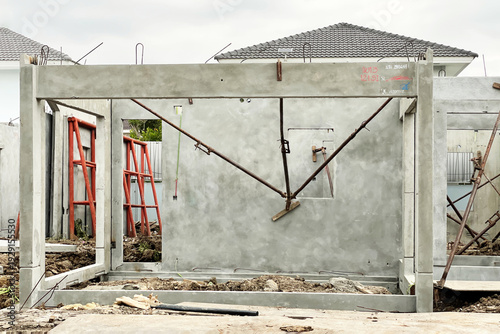 A wide shot of a residential building construction site featuring precast concrete wall panels and structural frames. The image shows the installation process with metal adjustable shoring props.