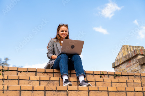 Urban woman working on a laptop outdoors on city steps.