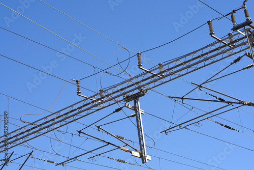 Low angle shot of complex overhead catenary power lines and steel support structures for electric trains set against a clear bright blue sky
