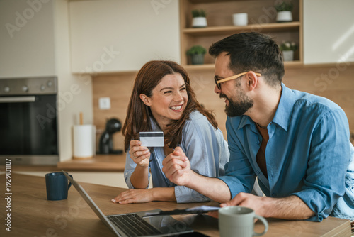 Foto Couple enjoying online shopping with credit card in kitchen
