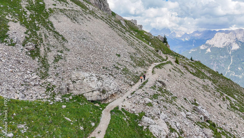 Aerial, bird view, hiking trail with some hikers, tourists along a mountain slope with grass and rocks,  near Rotwandhütte, Rifugio Roda di Vaèl mountain hut in Italian Dolomites. Beautiful hiking des