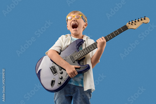 Little boy playing electric guitar on blue background