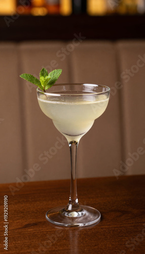 Light yellow cocktail with mint leaf garnish on a wooden table. Refreshing drink for happy hour. Beverage menu item at a bar