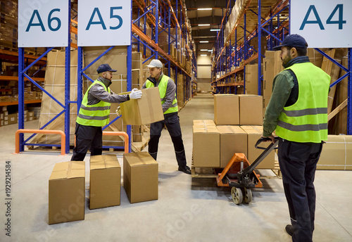 Schilderij op canvas Warehouse workers move boxes on pallet trolley