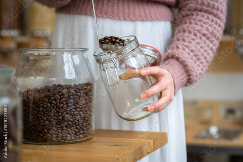 Close up of person refill a glass jar with fresh coffee beans from a bulk dispenser, promoting plastic-free living and sustainable shopping