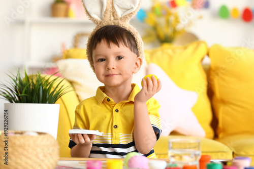 Cute little boy in bunny ears painting Easter egg at home