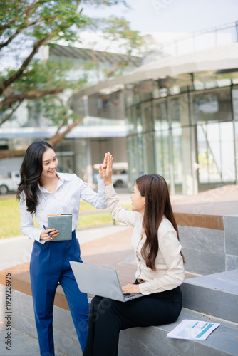 Asian businesswomen celebrating success with laptop outdoors, expressing teamwork, startup growth, achievement and corporate victory