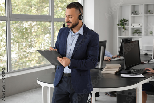 Male technical support agent with headset and clipboard in office