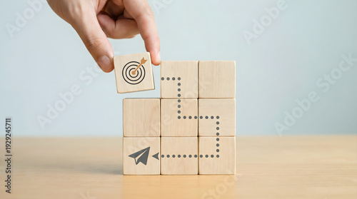 Hand placing target block on wooden cubes, symbolizing goal achievement and strategy