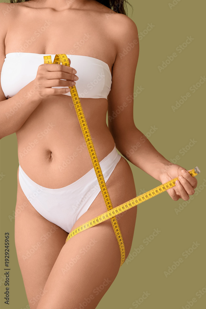 Fototapeta premium Beautiful young African-American woman with stretch marks on her body and measuring tape against green background, closeup