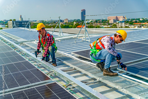 Fotografie Workers install solar panels on a rooftop in a city during daylight hours