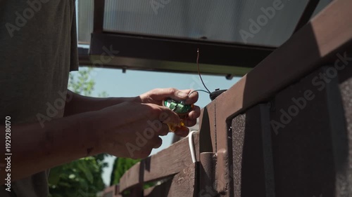 Close-up of electrician hands installing orange signal lamp on brick wall.