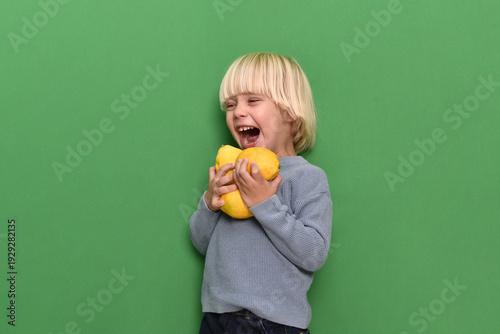 Little boy holding fresh lemons against green background, concept of healthy nutrition, vitamin C, immunity support and virus prevention. Child promoting natural food and strong immune system 