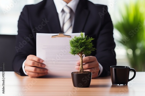 Man in formal suit holding a paper that features a detailed illustration of a tree design