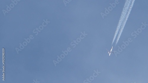 Tracking jet airliner flying through blue sky leaving white chemtrails