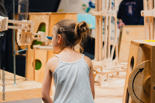 Young girl with brown hair observes interactive wooden exhibits in a modern museum space, showcasing educational play structures and creative designs for children