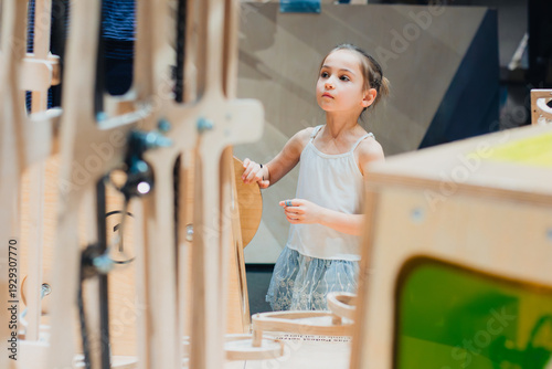 Young girl interacting with educational exhibits in an interactive museum, surrounded by wooden structures and colorful elements designed for hands-on learning experiences