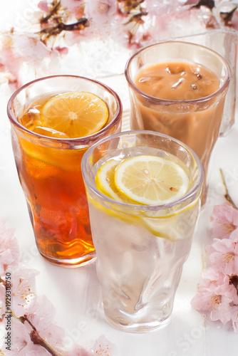 Three tall glasses of iced drinks: lemon tea, milk tea, and clear lemon water with slices.