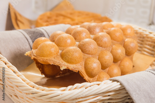 A golden egg waffle placed in a wicker basket lined with paper, showing its bubble-like texture.